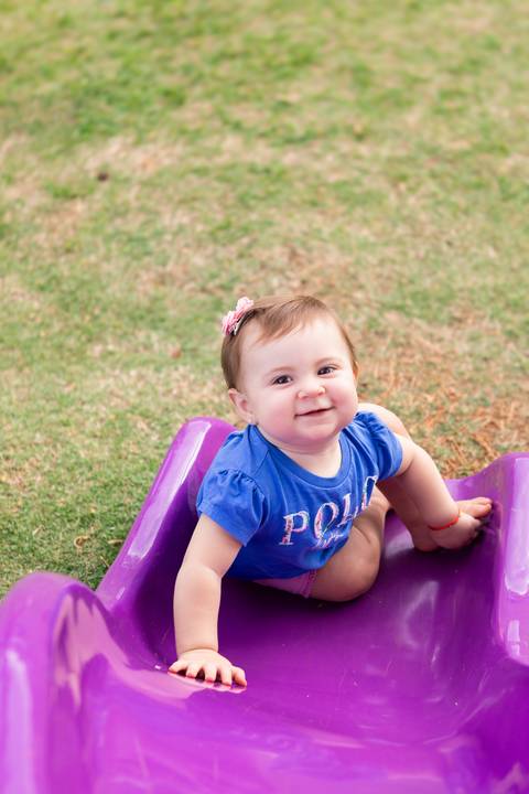 Autonomia e bem-estar infantil em atividades de lazer. Cecília descendo de forma divertida pelo escorregador colorido no gramado.'