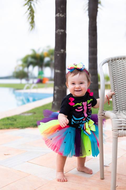 Momento lúdico e festivo no crescimento do bebê. Cecília com traje temático colorido e tiara de laço em comemoração familiar.'