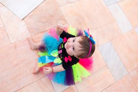 A delicadeza e o encanto do universo infantil. Visão aérea da bebê Cecília com vestido de tutu colorido em momento lúdico e descontraído.'
