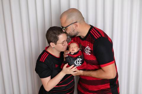 A alegria e as paixões familiares compartilhadas desde o berço. A recém-nascida Laura envolta em wrap temático do Flamengo em estúdio minimalista.'