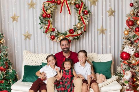 Proteção paterna e laços de amor na infância. O papai Leonardo em momento de carinho e sorrisos com os filhos em cenário iluminado de fim de ano.'