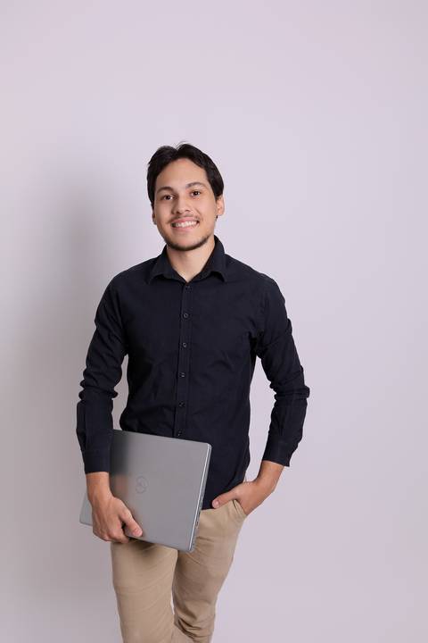 Retrato dinâmico para profissionais de TI e informática. Christopher segurando laptop em imagem estratégica que contextualiza sua área de atuação.'