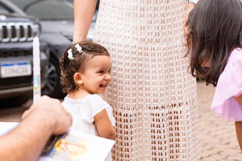 Desenvolvimento saudável e pura espontaneidade infantil. Aurora se divertindo ao ar livre com os pais após a cerimônia de batizado.'