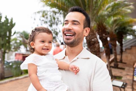 Desenvolvimento saudável e pura espontaneidade infantil. Aurora se divertindo ao ar livre com os pais após a cerimônia de batizado.'