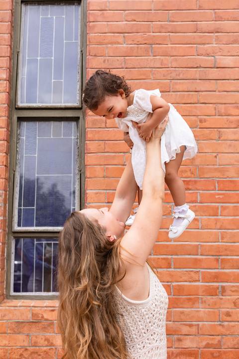 Desenvolvimento saudável e pura espontaneidade infantil. Aurora se divertindo ao ar livre com os pais após a cerimônia de batizado.'