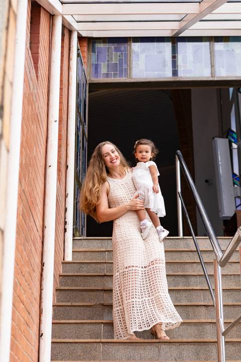 Desenvolvimento saudável e pura espontaneidade infantil. Aurora se divertindo ao ar livre com os pais após a cerimônia de batizado.'