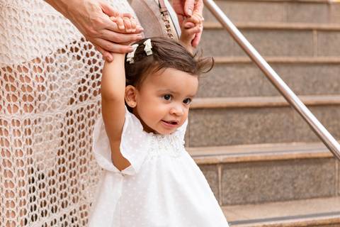 Desenvolvimento saudável e pura espontaneidade infantil. Aurora se divertindo ao ar livre com os pais após a cerimônia de batizado.'