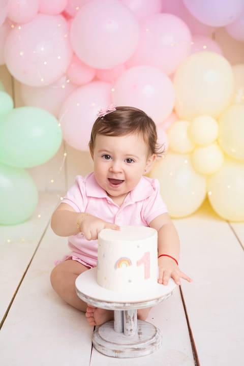 Fotografia infantil em estúdio minimalista. Registro afetivo de aniversário de um ano com balões em tons pastel.'