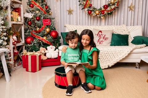 Desenvolvimento saudável, leitura e criatividade. Os irmãos Enrico e Letícia interagindo de forma lúdica no cenário de Natal.'
