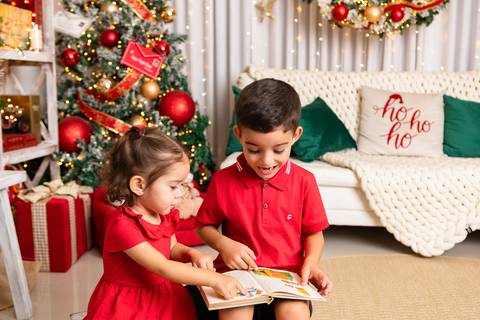 Desenvolvimento saudável, leitura e criatividade. Os irmãos João e Isabela interagindo de forma lúdica no cenário de Natal.'