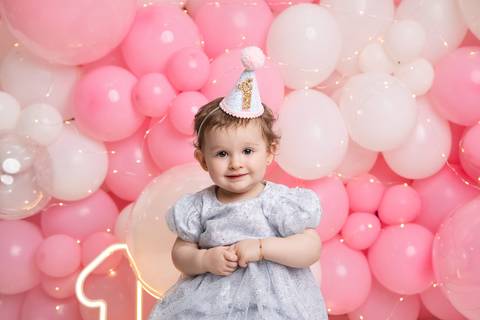 Expressões espontâneas e fofura do bebê de um ano. Maria Helena sorrindo com chapéu temático de aniversário no estúdio.'