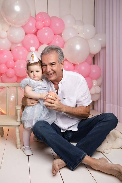 Conexão paterna e carinho no ensaio de um ano. Marcelo abraçando a filha Maria Helena em momento descontraído.'