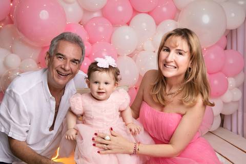 Retrato de família no estúdio em Brasília. Andrea, Marcelo e a filha de vestido rosa celebrando juntos.'