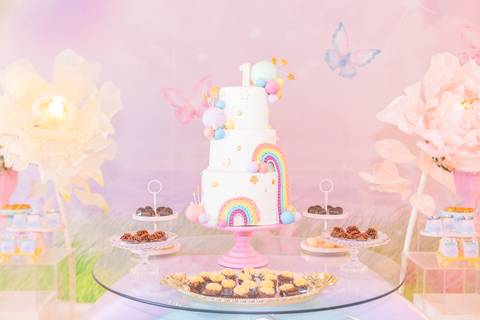 Bolo decorado para festa de um ano infantil. Detalhe de bolo temático com nuvens e arco-íris em tons suaves.'