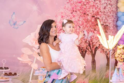 Conexão materna e carinho em festa de aniversário. Mariana sorrindo com a filha Cecília no colo em Brasília.'