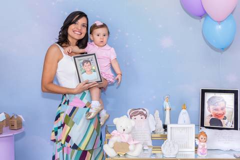 Recordação afetiva e passagem do tempo. Mariana segurando porta-retrato do filho ao lado da Cecília com um ano. Altar infantil.'