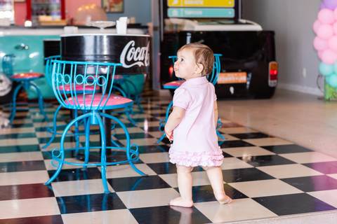 Fase de primeiros passos e desenvolvimento infantil. Cecília caminhando no salão de festas decorado em Brasília.'
