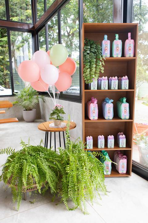 Mesa de lembranças para aniversário infantil em Brasília. Sacolas personalizadas expostas em estante de madeira.'