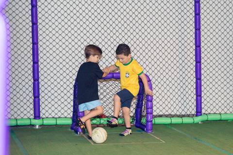 Atividades esportivas e brincadeiras em festa de aniversário. Crianças se divertindo jogando bola na quadra.'