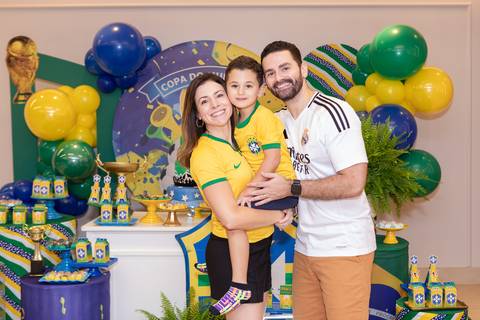Retrato oficial de família diante do bolo de aniversário temático da Seleção Brasileira.'