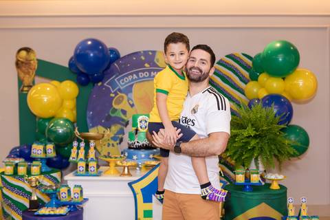 Proteção paterna e felicidade em família. Maurício carregando o aniversariante Lucas no colo no estúdio/buffet.'