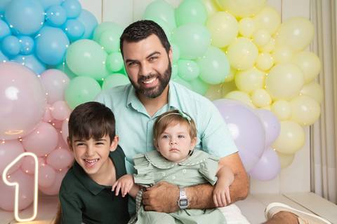 Momentos descontraídos em família. O pai Igor rindo e abraçando os filhos Pedro e Helena em cenário pastel.'