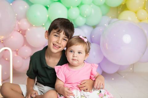 Carinho entre irmãos em ensaio fotográfico infantil em Brasília. Pedro e Helena sorrindo no estúdio.'