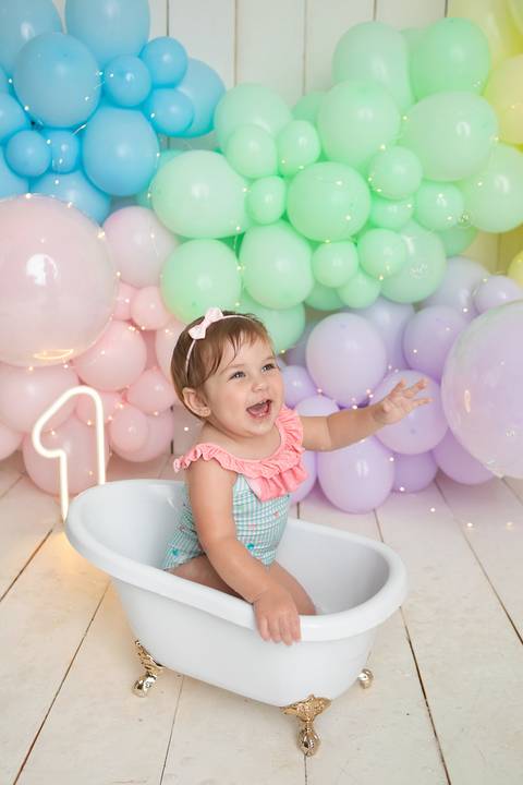 Registro completo de ensaio infantil de aniversário no estúdio. Helena na banheirinha em cenário de balões pastel.'