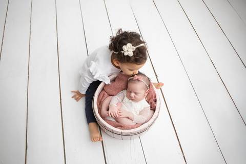 Ensaio fotográfico newborn com irmãos em Brasília. A irmã Amanda interagindo com a bebê Laura durante sessão de fotos afetiva no estúdio Letícia Franco Fotografia.'