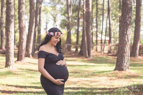 pinheiros e gestante no jardim botanico com vestido preto e coroa de flores brasilia df grávida book olhando para a barriga'