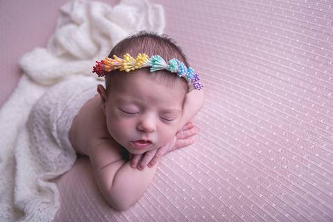 bebe recem nascido newborn book preço valor brasilia df pose mão no queixo mãozinha queixinho barriga pra baixo fundo rosa com branco e headband faixa cabelo arco-iris rainbow baby bebe tempestade felicidade paninho wrap branco por cima manta'