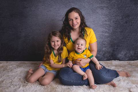 bebe book ensaio acompanhamento 06 07 meses fundo azul chão madeira caixinha de coração roupa azul de capuz sorrindo bebe sério tapete com a mamãe jeans e blusa branca irmã uniforme seleção brasileira futebol copa do mundo'