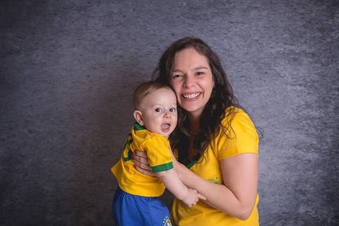 bebe book ensaio acompanhamento 06 07 meses fundo azul chão madeira caixinha de coração roupa azul de capuz sorrindo bebe sério tapete com a mamãe jeans e blusa branca irmã uniforme seleção brasileira futebol copa do mundo'