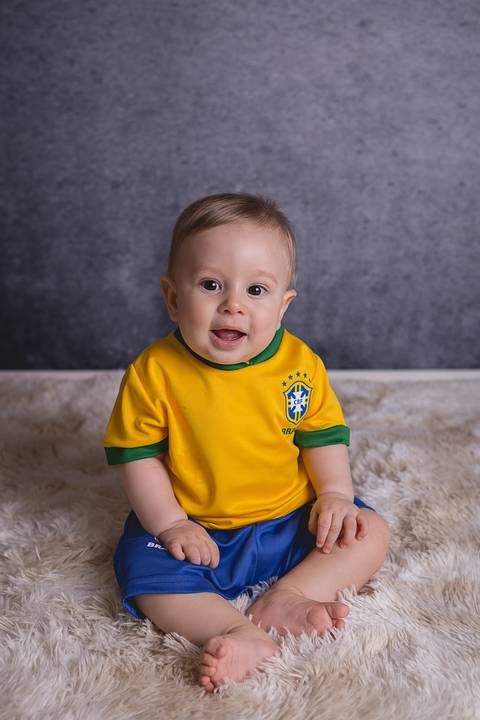 bebe book ensaio acompanhamento 06 07 meses fundo azul chão madeira caixinha de coração roupa azul de capuz sorrindo bebe sério tapete com a mamãe jeans e blusa branca irmã uniforme seleção brasileira futebol copa do mundo'