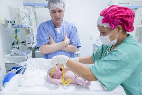 enfermeira medindo cabeça do bebê após o nascimento parto normal humanizado e pai observando emocionado'