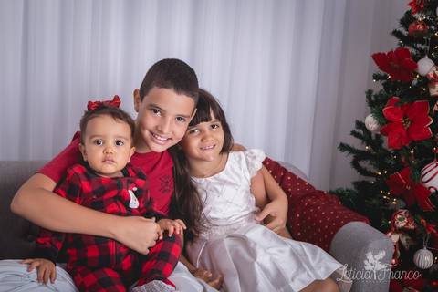 ensaio de natal infantil criança touca de papai noel 2019 brasilia df registrado pela fotógrafa letícia franco casa do papai noel cama arvore guirlanda sala irmãos'