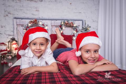 ensaio de natal infantil criança touca de papai noel 2019 brasilia df registrado pela fotógrafa letícia franco casa do papai noel cama arvore guirlanda sala irmãos'