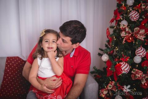 ensaio de natal bebê touca de papai noel 2019 brasilia df registrado pela fotógrafa letícia franco casa do papai noel sala arvore guirlanda roupa de papai noel giovanna com papai beijando e ela fazendo pose'