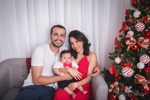 ensaio de natal bebê touca de papai noel 2019 brasilia df registrado pela fotógrafa letícia franco casa do papai noel sala arvore guirlanda roupa de papai noel pequeno romero de 3 meses com gravata borboleta e a mamãe rayssa e o papai bruno'
