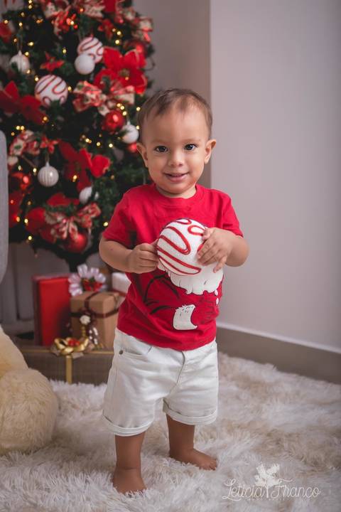 ensaio de natal bebê touca de papai noel 2019 brasilia df registrado pela fotógrafa letícia franco casa do papai noel sala arvore guirlanda roupa de papai noel com a bola de natal na mão'