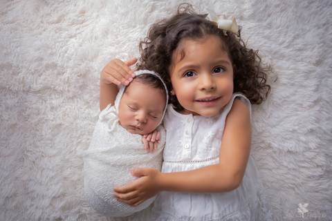 bebê recém nascido newborn brasilia fotografa fotografo fotógrafa brasília df distrito federal baby bebe reborn book melhor leticia franco menino e irmã abraçando sorrindo no fundo branco enroladinho no wrap tecido branco vestido branco'