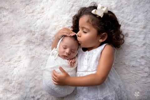 bebê recém nascido newborn brasilia fotografa fotografo fotógrafa brasília df distrito federal baby bebe reborn book melhor leticia franco menino e irmã beijando a cabeça do bebê, enroladinho no wrap tecido branco fundo branco vestido branco'