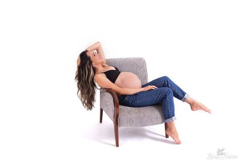 ensaio gestante mamãe fotografa fotógrafa brasília df distrito federal baby bebe reborn book melhor leticia franco letícia estúdio  gestante com a mão no cabelo e na barriga ligerie preta fundo branco  sentada na poltrona sorrindo com a mão no cabelo e de'
