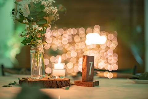 Alt Text: a imagem mostra uma mesa decorada com um vaso de vidro com flores brancas, uma vela e um ormanento de madeira com o número 7'