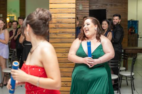 Alt text: a foto mostra as formandas entrando no salão sorrindo, uma vestindo um vestido longo verde e a outra um vestido vermelho'