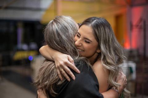 Alt text: duas mulheres se abraçando sorrindo, elas estão de cabelo solto e sorrindo'