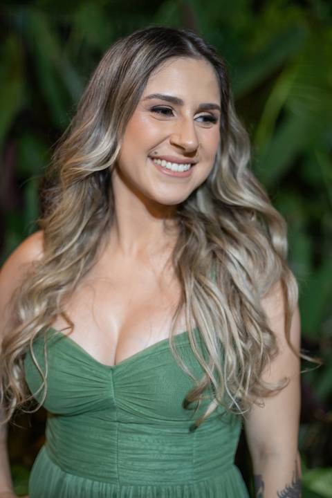 Alt text: formanda posando com vestido verde e sorrindo com folhagens verdes de fundo'