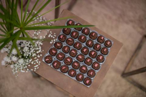 Alt text: forma com brigadeiros com chocolates rosa em cima, e uma folhagem decorativa ao lado'