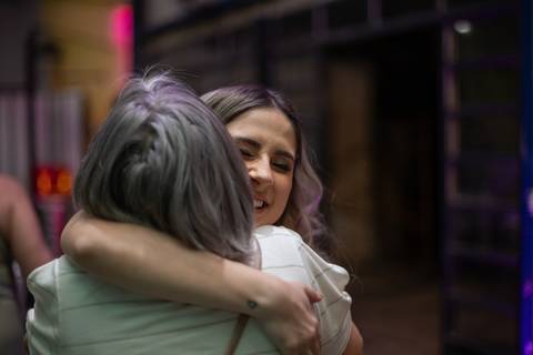 Alt text: duas mulheres se abraçando sorrindo, elas estão de cabelo solto e sorrindo'