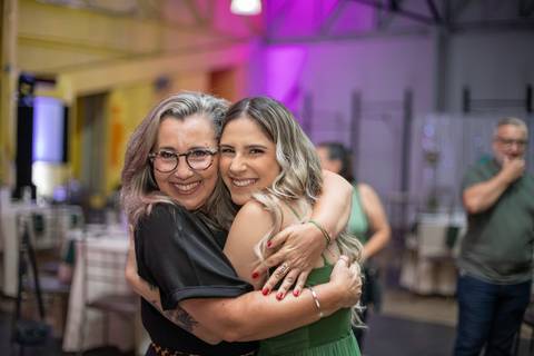 Alt Text: duas mulheres se abraçando e sorrindo em um ambiente de formatura decorado'